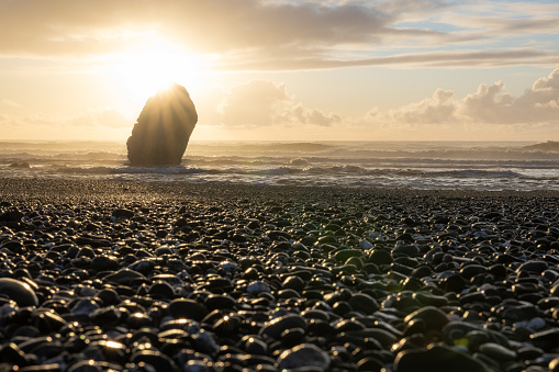 A rocky beach with a large rock in the foreground. The sun is shining on the rock, creating a beautiful and serene atmosphere