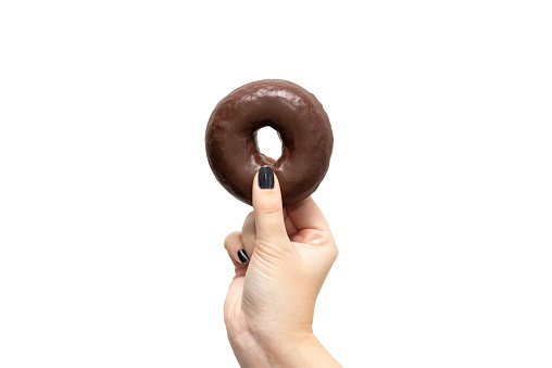 Close-up detail of a woman's hand holding a chocolate doughnut in her fingers against a white background