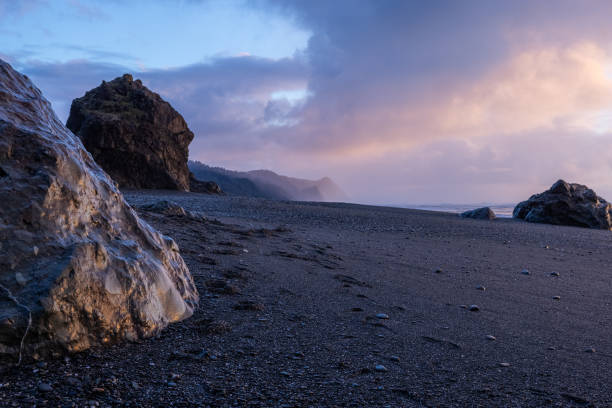 a rocky beach with a large rock in the foreground - beauty in nature cloud rocky coastline rock foto e immagini stock