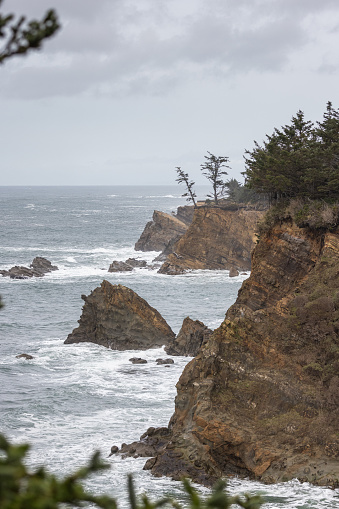 A rocky shoreline with a large body of water in the background. The water is choppy and the rocks are jagged. The sky is overcast and the mood of the image is somewhat ominous