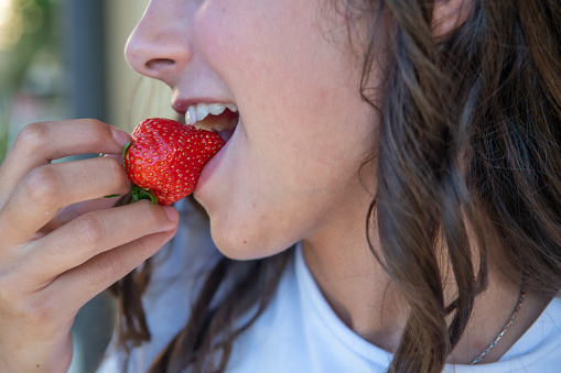 A young girl eating strawberries, detail on the mouth.