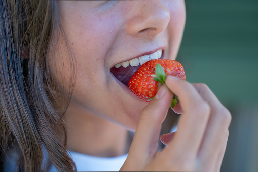 Vegetarian Food. A young girl eating strawberries, detail on the mouth.
