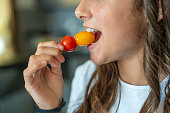 Vegetarian food. A young girl eating red and yellow tomatoes, detail on the mouth