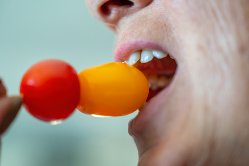 A woman eating yellow and red tomatoes, detail on the mouth.