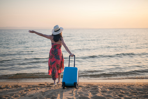 Happy young woman with suitcase on a summer vacation by the seaside.