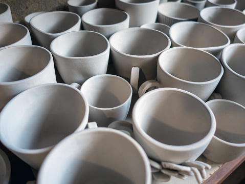Variety of unfinished earthenware cups stand on a simple wooden shelving unit