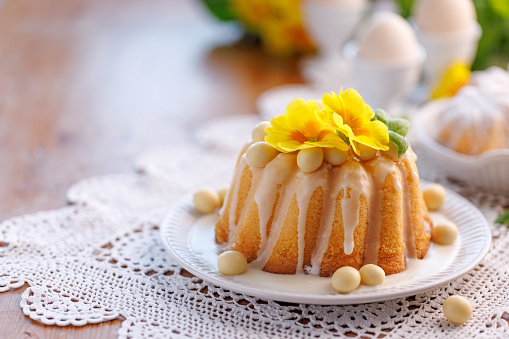 Easter bundt cake, Babka covered with icing, decorated with chocolate eggs and primrose flowers on a festive table, with copy space. Traditional dessert