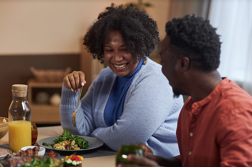 Portrait of adult African American couple chatting at dinner table in cozy home and smiling happily