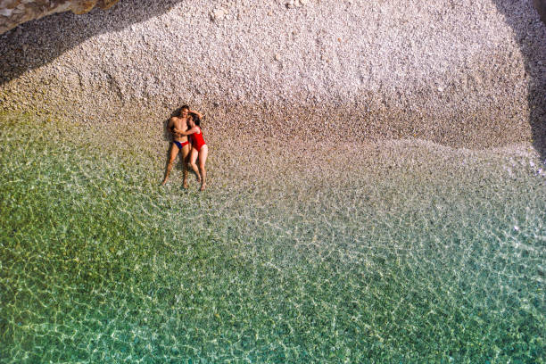 Couple enjoying vacation and relaxing alone on the beautiful beach.  Young woman and man in love sunbathing and color of water is amazing. Filiatro beach, Ithaca Island, Greece