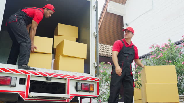 Delivery man stand on truck and send parcel or box to his co-worker during transport the product to customer house.