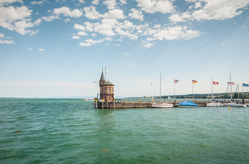 Konstanz, Germany - August 04 2013: old lighthouse on the end of stone mole in Konstanz harbor. Few sailboats moored to the pier. Beautiful view of lake Constance, blue sky in the background.