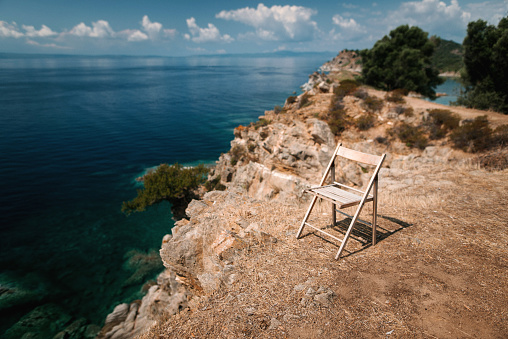 Free empty wooden chair standing on the rocky cliff with beautiful sea view. Sunny summer day in Greece