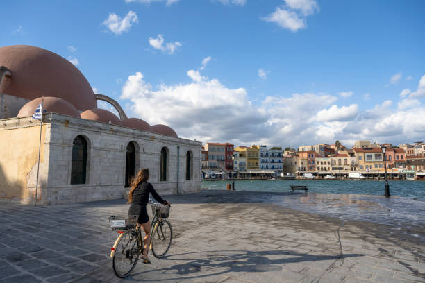 Woman explores old harbour with bicycle, looks off to city in distance