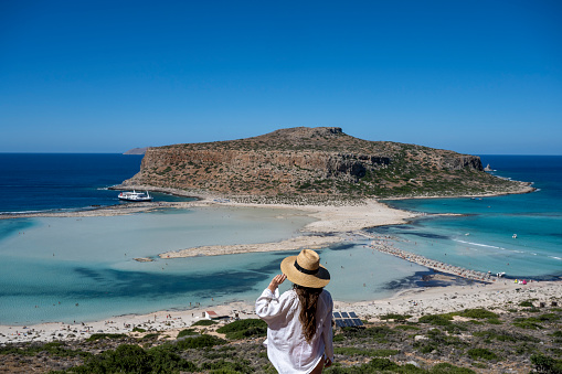 Woman wearing hat looks down to calm bay and island