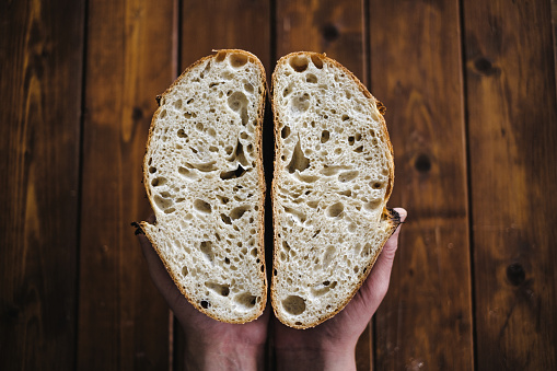 Female hands close-up breaking fresh baguette bread. Warm old french room in background. Hands tearing apart loaf.