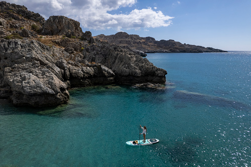 Aerial view of woman stand up paddle boarding on calm bay, Southern  Crete
