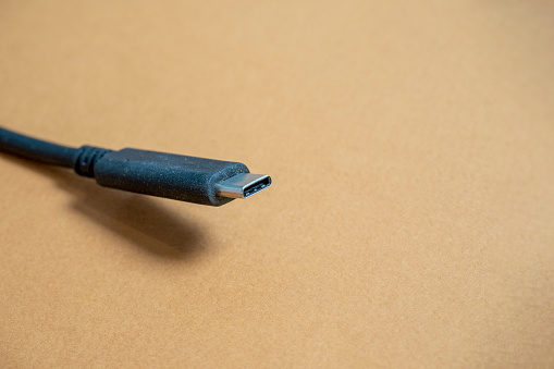 Black usb type C cable on brown background. Copy space, a place for the text. Selective focus. Communication cable for connecting equipment and data transmission