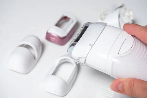 Photo of an electric epilator in a woman's hand.In the background, the various nozzles are out of focus. Devices for women's beauty