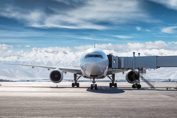 frontansicht des weißen großraum-passagierflugzeugs auf der luftbrücke auf dem flughafenvorfeld vor dem hintergrund hoher schneebedeckter berge - airfield mountain snow airport stock-fotos und bilder