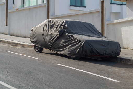 An awning covering a parked car by the side of the road. Protecting the vehicle from the harmful effects of direct hot sunlight and from the gaze of passers-by