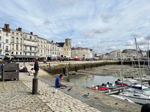 People sitting on the. harbour wall at La Rochelle, in France. September 2022