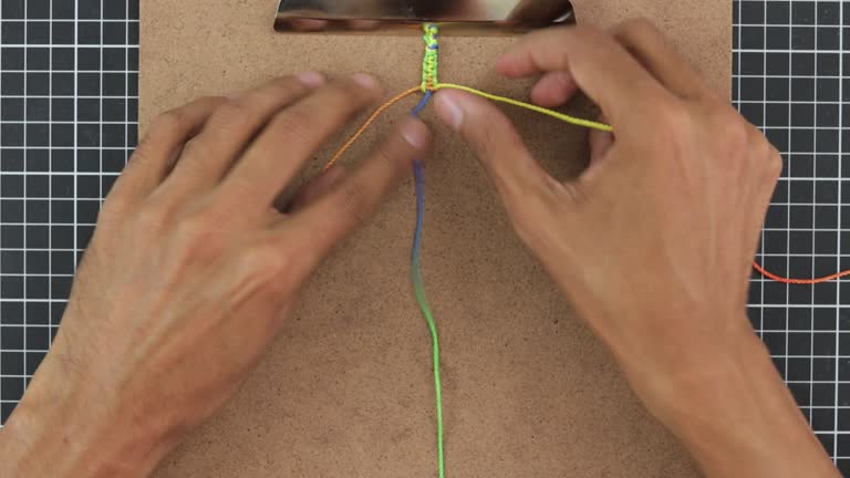 hands threading three strings together to create macrame bracelet.