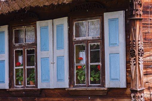 Window with yellow shutters on the facade of an old wooden cottage