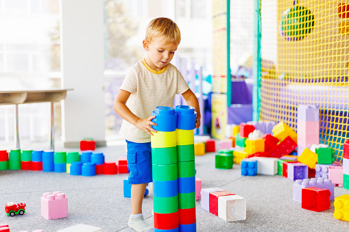 Child playing with colorful building blocks in a playroom setting. Kids' educational toys concept with bright primary colors for design and print