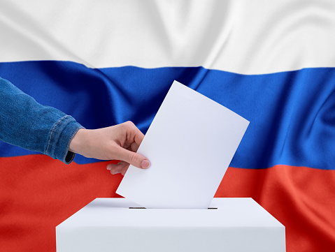 Elections, Russia. A human hand throws a ballot into the ballot box. The flag of Russia on the background.