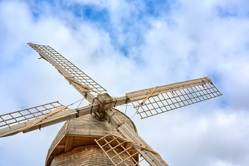 Wooden windmill wings close-up against the sky with clouds. Axle of a wooden mill with wings.