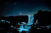 Stars on the dark blue sky above Thingevllir Natural Reserve in Iceland with a Öxarárfoss waterfall