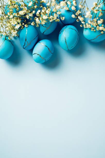 istock Elegant Easter eggs with spring flowers on pastel blue background. Vertical, flat lay, top view. 2081691650