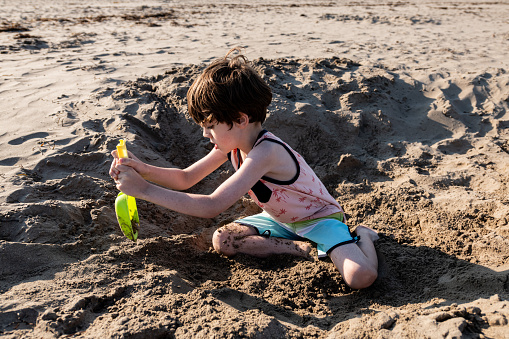 A boy enjoys digging a deep hole at a beach.