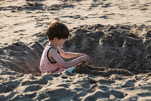 A boy enjoys digging a deep hole at a beach.