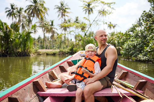 A father sits with his son on a longtail boat during a trip on a canal in Thailand