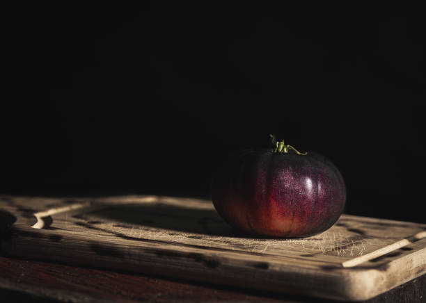 organic blue tomato, illuminated from the side by a soft light coming through a window, on wooden plank, copy space
