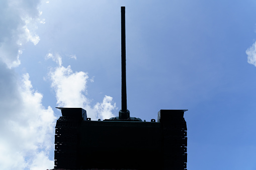 A sharp silhouette of the tank is shown, emphasizing the shape of the turret and hull against a blue sky with clouds.