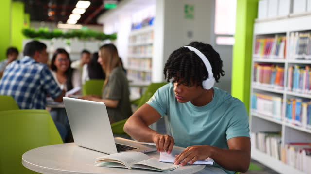 African American student studying at a public library using a laptop and headphones