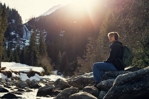 teenage boy sitting on rock by the river in the austrian alps - river stones audio fotografías e imágenes de stock