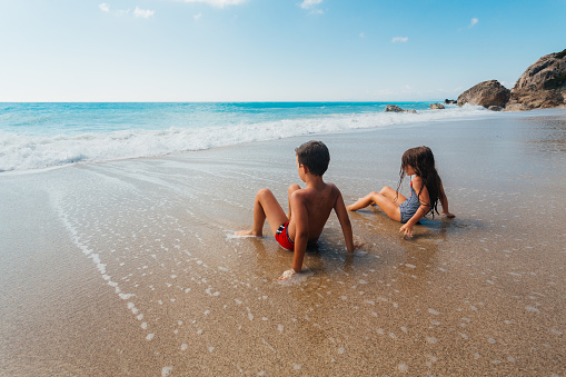 Siblings having fun catching the waves on a beautiful beach on the Greek Lefkada island