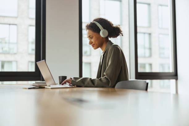istock A woman with headphones sits at a table using a laptop computer in nice modern coworking office 2081885044