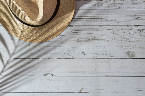 Top view of white painted wooden planks with straw hat and palm tree shadow