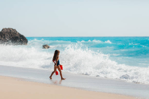 Little girl having fun running and playing on the waves on a beautiful beach on the Greek Lefkada island