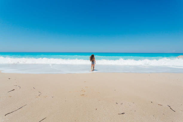 Little girl having fun running and playing on the waves on a beautiful beach on the Greek Lefkada island