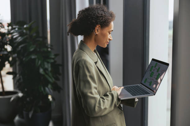 istock Woman in formal wear standing by a window using a laptop computer 2081917599
