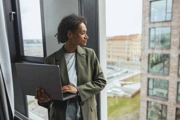 istock a woman is using a laptop computer while looking out of a window 2081923004