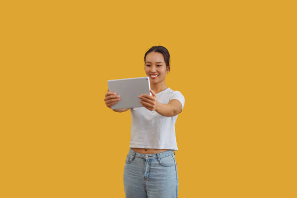 istock Cheerful beautiful woman taking selfie with digital tablet while standing in front of yellow background 2081925384