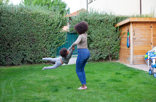 Happy African mother whirl her son, having fun with a child in backyard