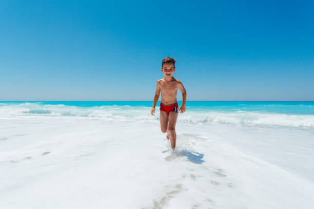 Teenage boy enjoys summer vacation running and jumping on the waves at a beautiful beach on the Greek Lefkada island