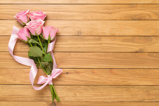 Pink roses on wooden background, top view.